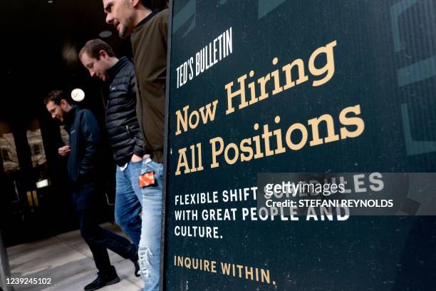Pedestrians walk past a Now Hiring sign in Arlington, Virginia, on March 16, 2022. - The US unemployment rate has fallen to below four percent, but...