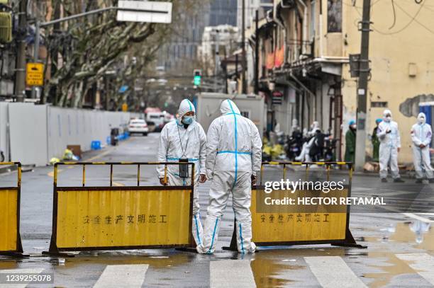 Workers wearing protective gear stand next to barriers placed to close off streets around a locked down neighbourhood after the detection of new...