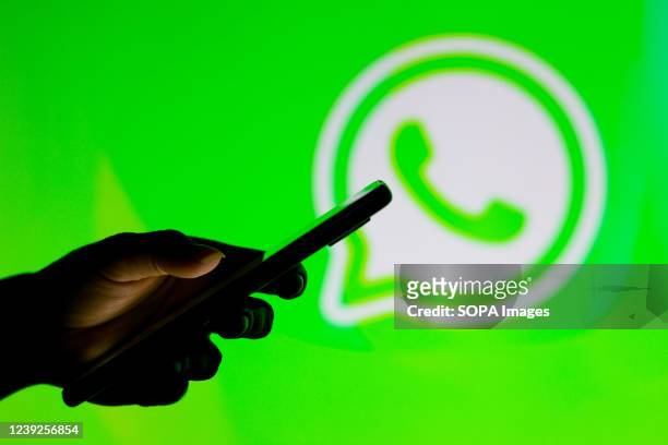 In this photo illustration the WhatsApp logo seen in the background of a silhouette woman holding a mobile phone.
