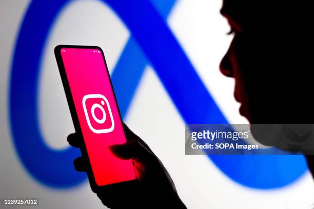 In this photo illustration, a woman holds a smartphone with the Instagram logo displayed on the screen with the Meta Platforms logo displayed in the...