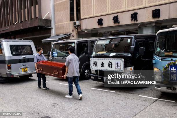 Two men carry an empty coffin past a row of hearses outside a funeral parlour in the Kowloon district of Hong Kong on March 17, 2022. - A funeral...