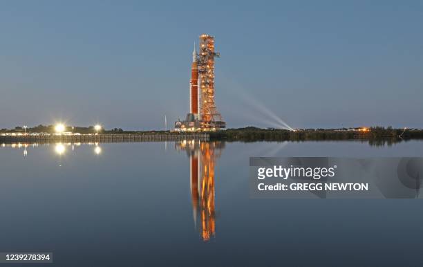 The massive Artemis I rocket is illuminated at dusk atop a mobile launch platform en route to Launch Pad 39B from the Vehicle Assembly Building at...