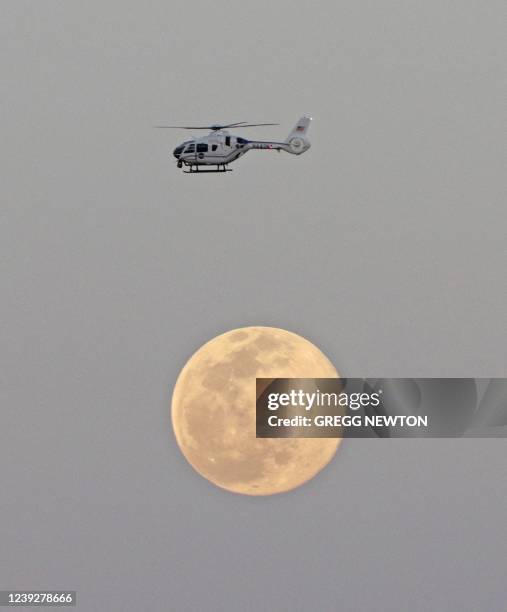 Helicopter flying near the Artemis I rocket soars past a full moon during the rollout to Launch Pad 39B from the Vehicle Assembly Building, at the...