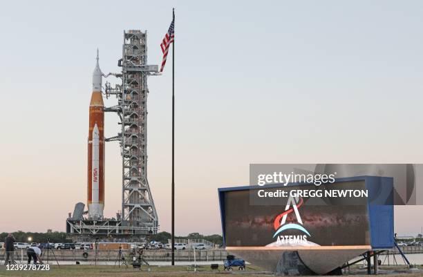 The massive Artemis I rocket rolls past the countdown clock atop a mobile launch platform en route to Launch Pad 39B from the Vehicle Assembly...