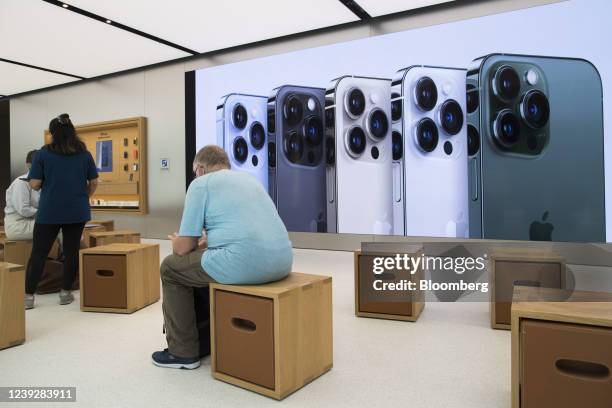 Customer sits in front of an advertisement for Apple Inc. IPhone 13 Pro smartphones at one of the company's stores in Sydney, Australia, on Friday,...