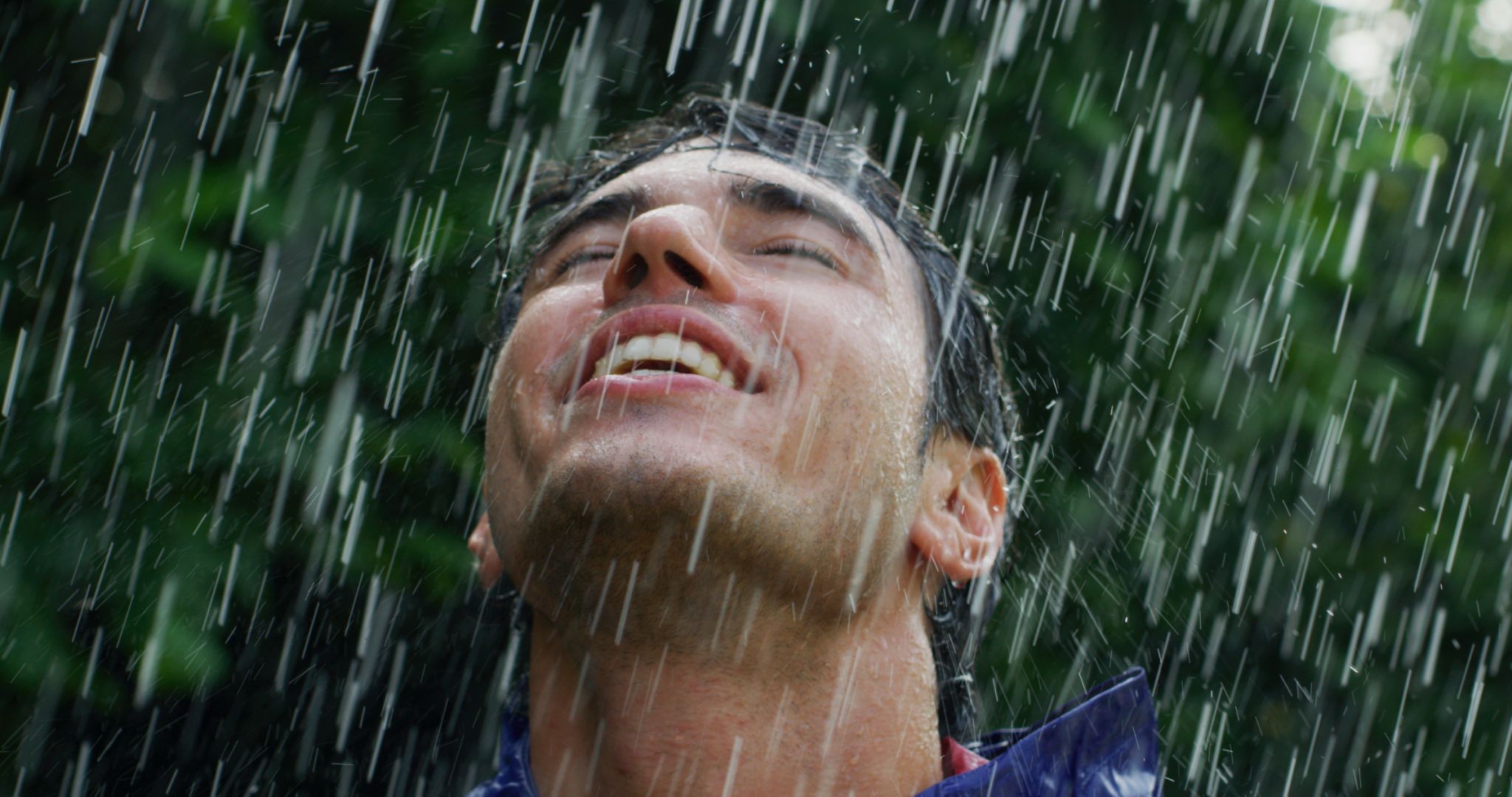 Portrait of young carefree handsome young man wearing protection cape is feeling free under the rain on a background of green trees. Portrait of young carefree handsome young man wearing protection cape is feeling free under the rain on a background of green trees.