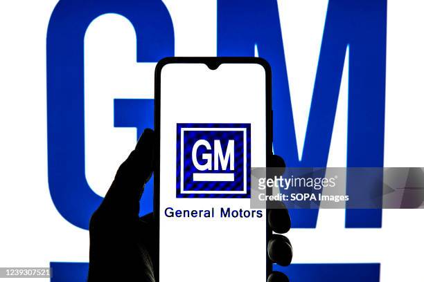 In this photo illustration a General Motors Company logo seen displayed on a smartphone with a General Motors Company logo in the background.