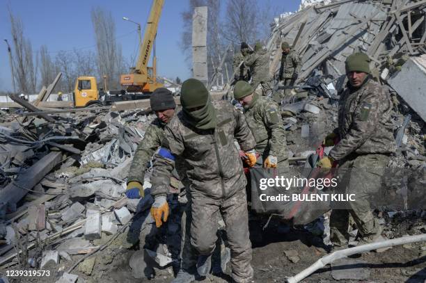 Graphic content / TOPSHOT - Ukrainian soldiers carry a dead soldier through debris at the military school hit by Russian rockets the day before, in...