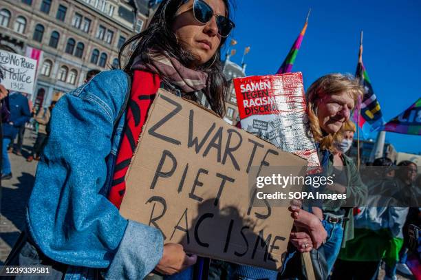 Woman is seen holding a placard against the figure of Black Peter, who is usually a white person with black paint in his face during the...