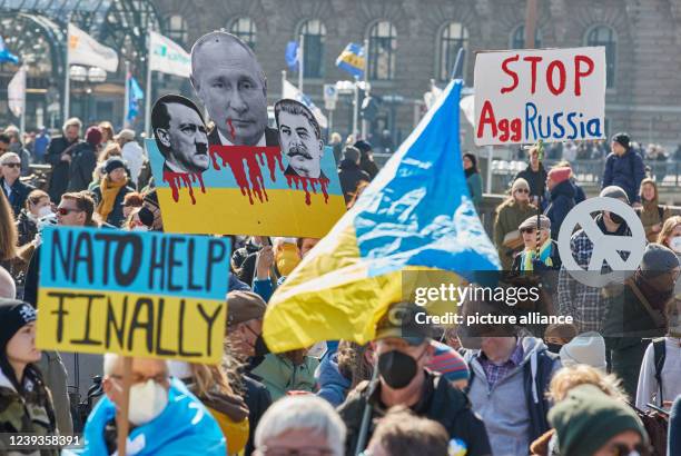 March 2022, Hamburg: Participants of the demonstration "Peace in Ukraine - Security in Europe" hold banners with the peace sign and with the...