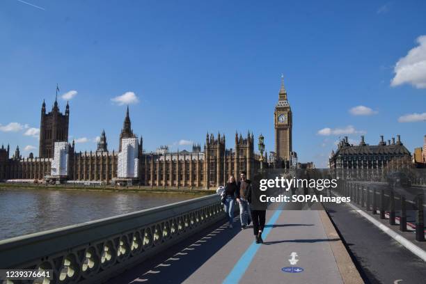 People walk across Westminster Bridge past the Houses of Parliament and Big Ben on a clear day.