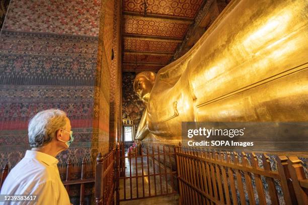 Foreign tourist wearing a face mask admires the large gilded statue of the Reclining Buddha in Wat Pho. Wat Pho is a Buddhist temple in the Phra...