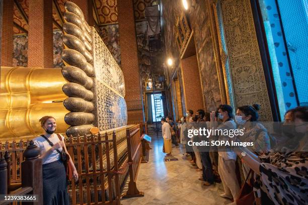 Foreign tourist poses for a picture next to the large gilded statue of the Reclining Buddha's foot in Wat Pho. Wat Pho is a Buddhist temple in the...