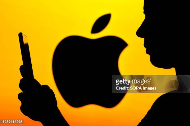 In this photo illustration, the Apple Inc logo is seen in the background of a woman's silhouette holding a mobile phone.