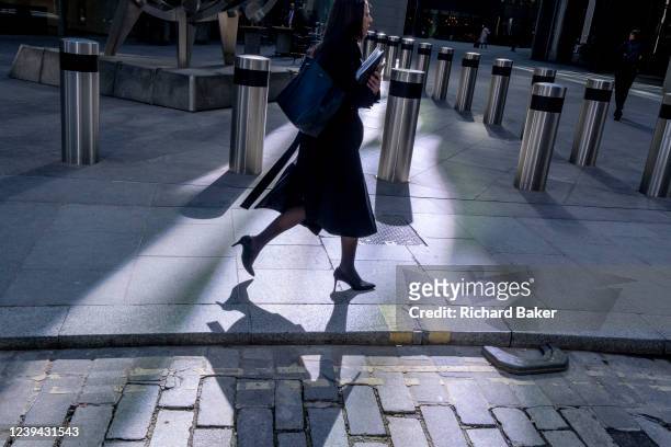 Woman walks through sunlight in Lime Street where many financial servioces and insurance companies have their headquarters in the City of London, the...