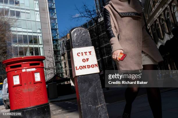 Carrying her phone and train ticket, an anonymous woman walks past a City of London bollard near Fenchurch Street Station in the City of London, the...