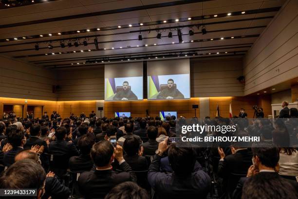 Members of Japan's lower house of parliament applaud as Ukrainian President Volodymyr Zelensky appears on a screen via video link at the House of...