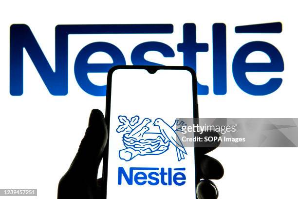 In this photo illustration a Nestle logo seen displayed on a smartphone with a Nestle logo in the background.