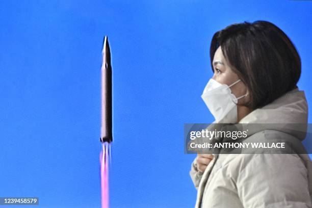 Woman walks past a television report showing a news broadcast with file footage of a North Korean missile test, at a railway station in Seoul on...