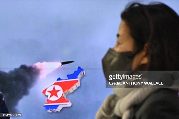 Woman walks past a television report showing a news broadcast with file footage of a North Korean missile test, at a railway station in Seoul on...