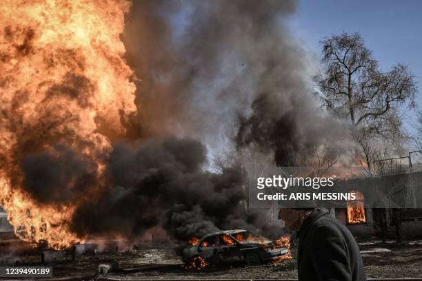 Ukrainian woman walks past flames and smoke rising from a fire following an artillery fire on the 30th day of the invasion of Ukraine by Russian...