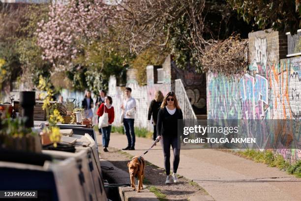 People walk beside Regent's Canal in the Spring sunshine in Victoria Park in east London on March 25, 2022. - Temperatures are well above the average...