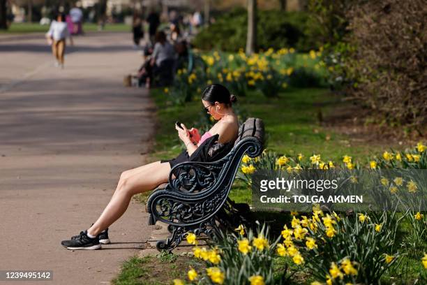 Woman relaxes beside daffodils in the spring sunshine in Victoria Park in east London on March 25, 2022. Temperatures are well above the average on...