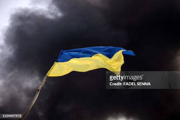 Ukrainian national flag waves while smoke rises after Russian attacks hit a fuel storage facility in the city of Kalynivka, on March 25, 2022.