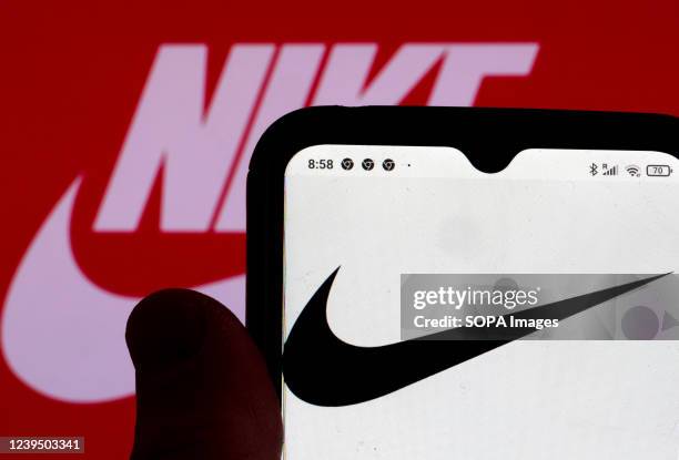 In this photo illustration, the Nike logo is displayed on a smartphone screen and in the background.