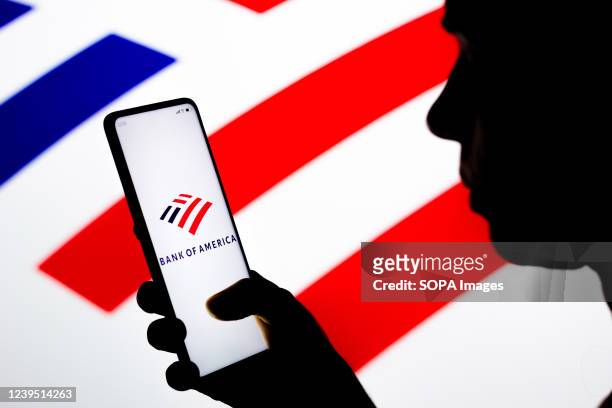 In this photo illustration, a woman's silhouette holds a smartphone with the Bank of America logo on the screen and in the background.