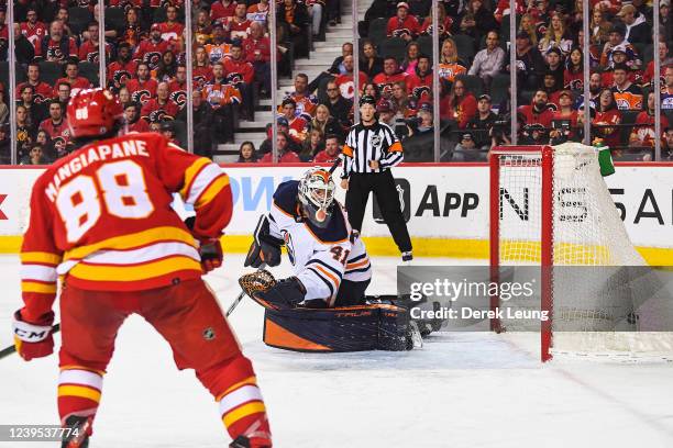 Andrew Mangiapane of the Calgary Flames watches the shot of his teammate Elias Lindholm fly past Mike Smith of the Edmonton Oilers during the third...