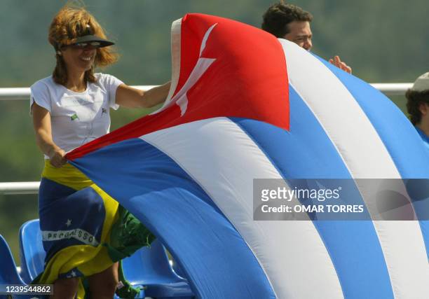 Fan wearing a Brazilian flag as a skirt struggles to handle a waving Cuban flag during the first round baseball game between Cuba and Mexico at...