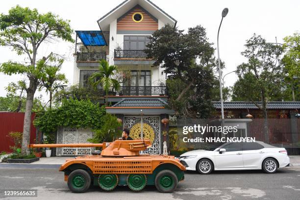 Truong Van Dao rides past a house in a wooden tank made from the conversion of an old minibus in a residential area in Bac Ninh province on March 28,...