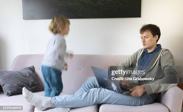 In this photo illustration a father with child is working on sofa on March 20, 2022 in Bonn, Germany.