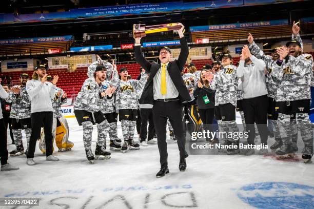 Adrian Bulldogs head coach Adam Krug raises the trophy during the NCAA Divison III Men's Ice Hockey Championship held at the 1980 Rink Herb Brooks...