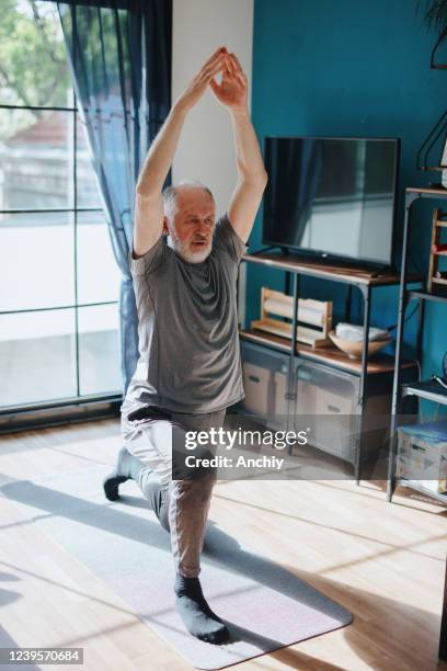 aktiver senior mann, der yoga zu hause praktiziert - senior yoga stock-fotos und bilder
