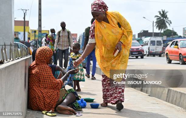 Pedestrian gives mony to a Nigerien woman sitting on the sidewalk with her children in Abobo suburb of Abidjan on March 28, 2022. - Many Nigerien...