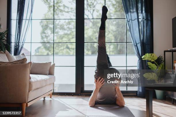 aktiver reifer mann, der zu hause beinddehnungsübungen macht - senior yoga stock-fotos und bilder