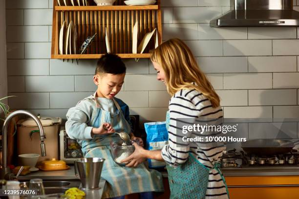 mother helping son to put flour into bowl - adoption photos et images de collection