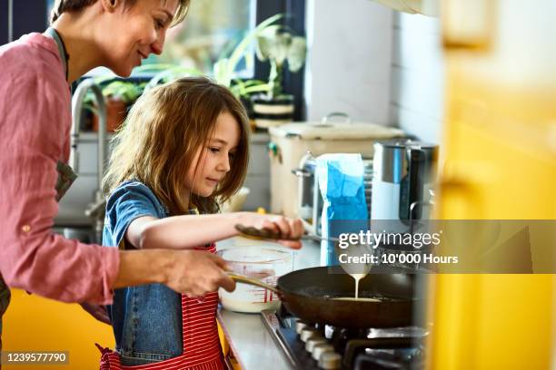 girl pouring pancake batter in frying pan, with mother - pancake day foto e immagini stock