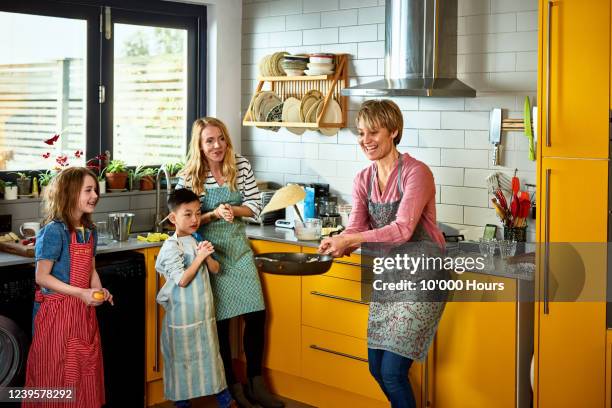 mother flipping pancake in kitchen with family - pancakes stockfoto's en -beelden