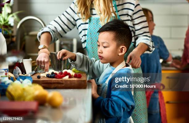 boy making fruit salad in kitchen with mother - asian family cooking stock pictures, royalty-free photos & images