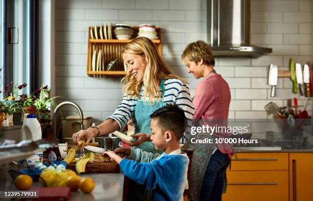same sex couple cooking with son in kitchen - lesbiana fotografías e imágenes de stock