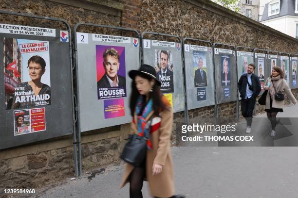 Pedestrians walk by official campaign posters of the 12 presidential candidates outside a school which will be used as a polling station in Paris, on...