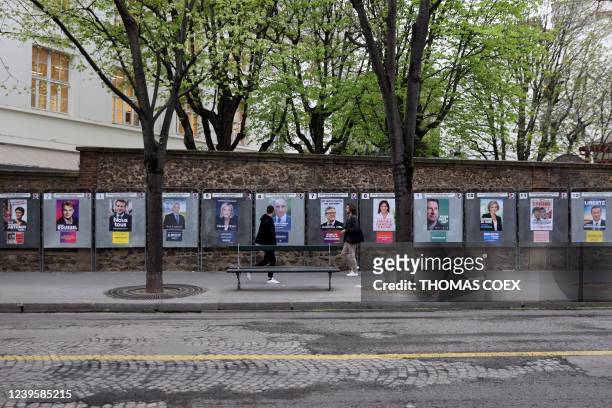 Pedestrians walk by official campaign posters of the 12 presidential candidates outside a school which will be used as a polling station in Paris, on...