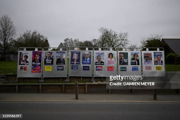 This picture, taken on March 29, 2022 shows presidential candidates posters on a billboard in La Baussaine, western France. - March 28, 2022 marked...