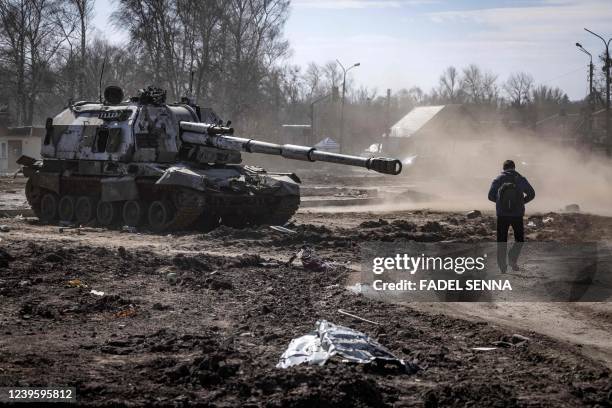 Resident walks near a damaged Russian tank in the northeastern city of Trostyanets', on March 29, 2022. - Ukraine said on March 26, 2022 its forces...