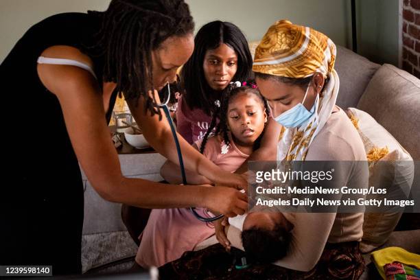 Aysha-Samon Stokes and her daughter Nyla watch Midwife Allegra Hill and student Midwife Maryam Karim take the heartbeat of two-week-old Nikko during...