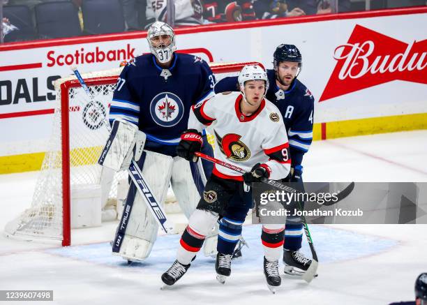 Josh Norris of the Ottawa Senators keeps an eye on the play in front of goaltender Connor Hellebuyck and Josh Morrissey of the Winnipeg Jets during...