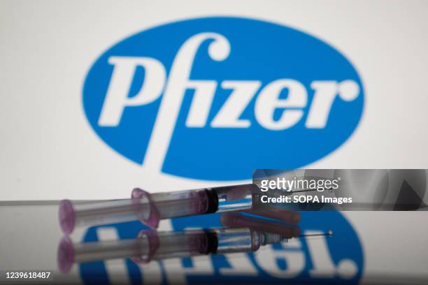 In this photo illustration, a medical syringe is displayed on a screen, and the logo of Pfizer in the background.